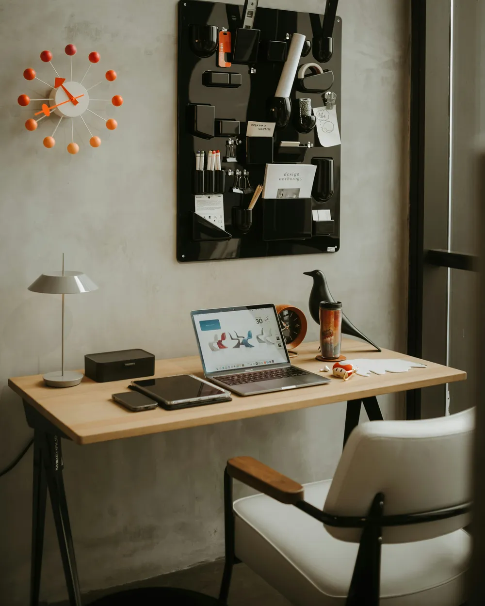 Escritorio de trabajo con portátil, lámpara y panel de notas en una pared de hormigón